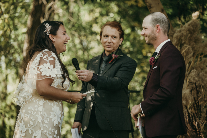 wedding officiant hands mic to laughing bride